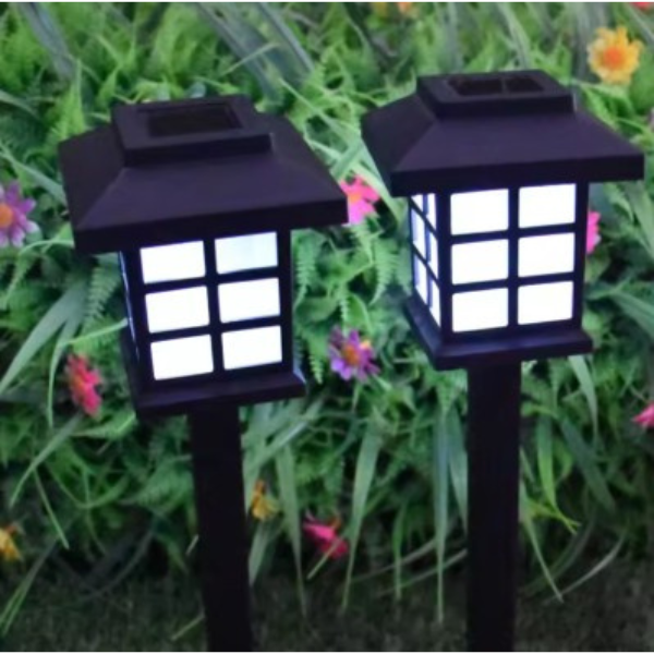 dwie solarne lampy LED zimne białe światło w trawie przy żywopłocie.png